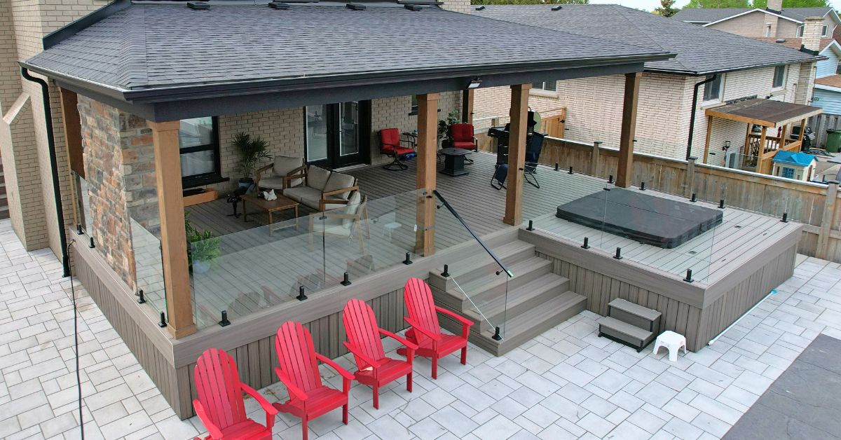 Frameless glass deck railing with black spigots along a backyard deck