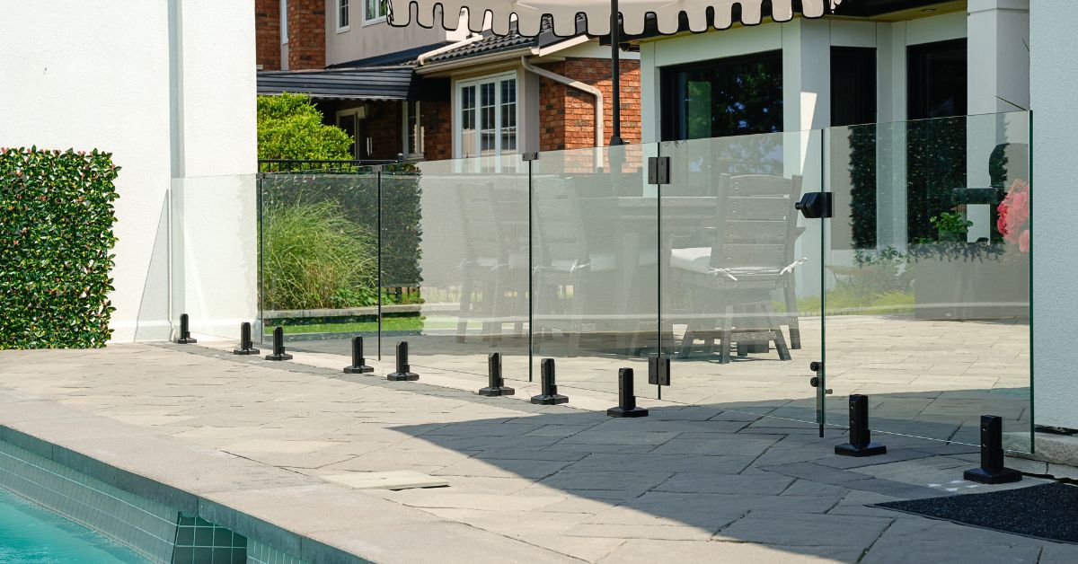 Frameless glass pool fence with black spigots around a backyard pool and patio