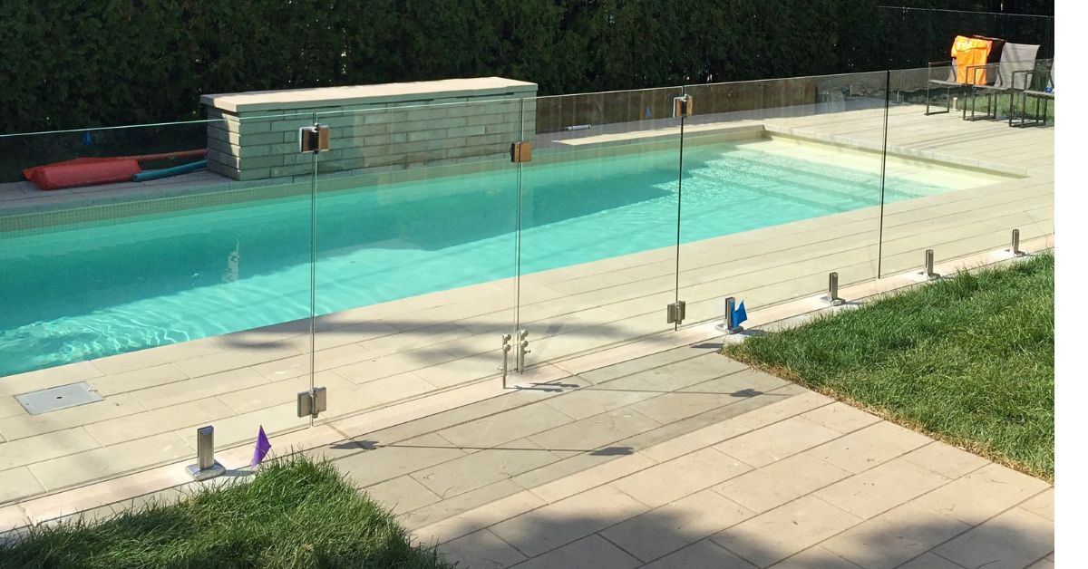 Frameless glass pool fence around an in-ground pool on a concrete patio