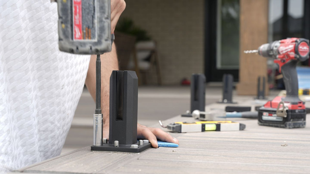 Installer mounting a black base shoe to a composite deck with a cordless drill