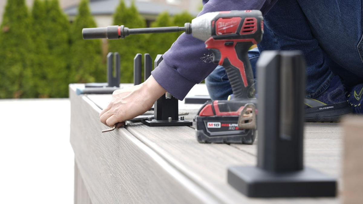 Installer tightening glass railing hardware with an impact driver during final inspection